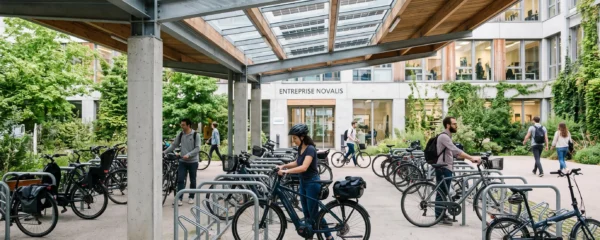 Des salariés garent leurs vélos dans un parc à vélos couvert devant leur entreprise.